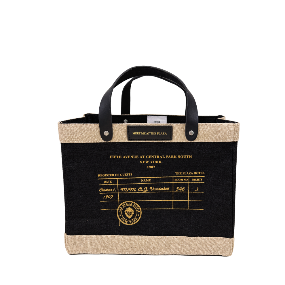 A tote bag with a black body, natural jute trim, and black leather handles. The front features a printed vintage hotel guest register design in gold with the text 'FIFTH AVENUE AT CENTRAL PARK SOUTH NEW YORK 1907' and a gold 'The Plaza Hotel New York' emblem.