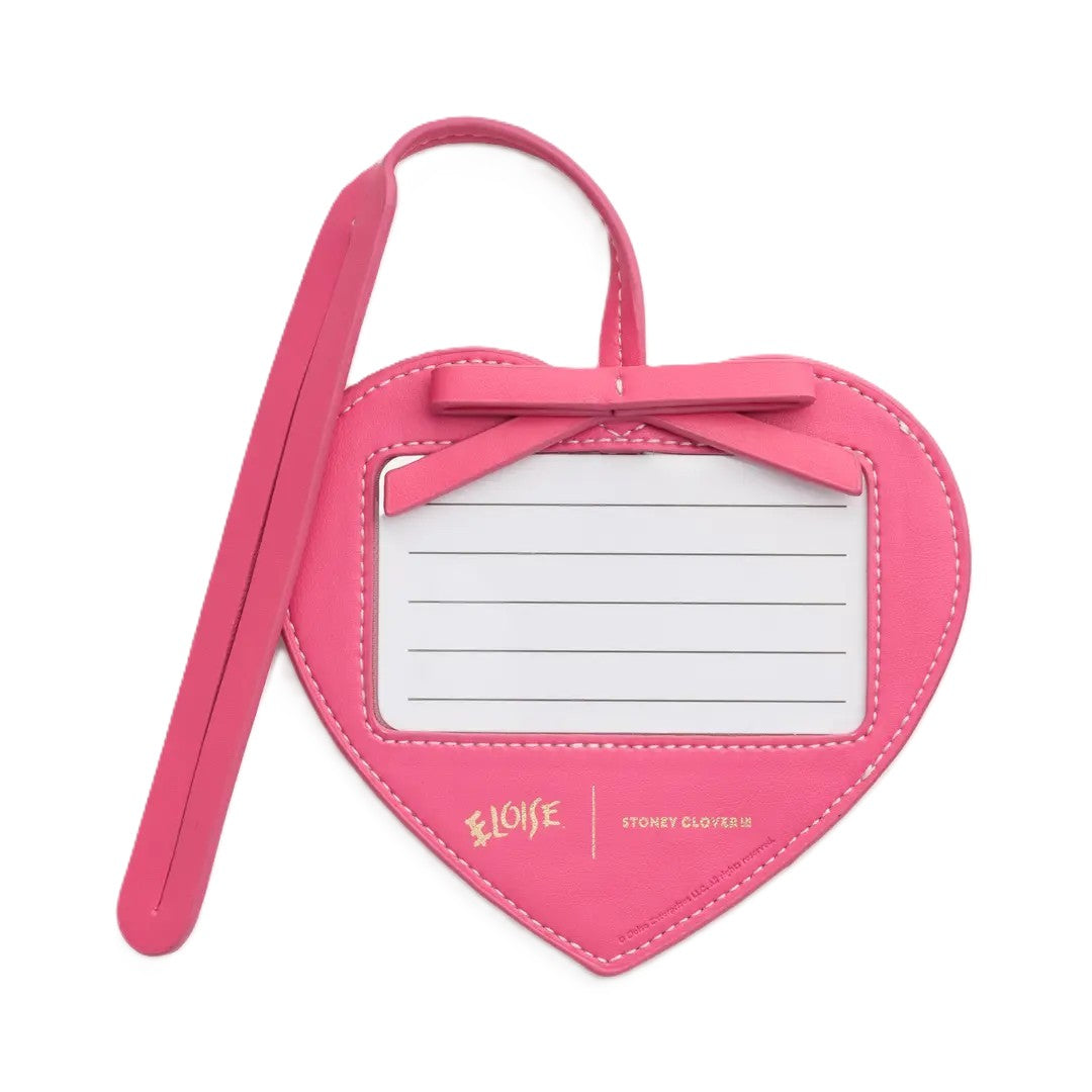 A bright pink heart-shaped luggage tag with a matching pink strap, a bow on top, and a white identification panel with gold text reading 'ELOISE' and 'STONEY CLOVER II'.