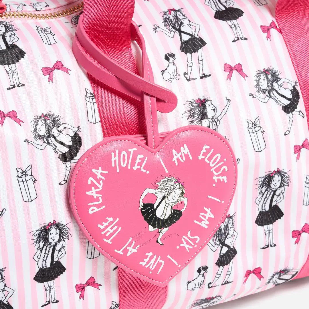 A close-up of a pink and white striped duffel bag with a bright pink heart-shaped luggage tag attached. The tag features the text 'I AM ELOISE I AM SIX I LIVE AT THE PLAZA HOTEL' and an illustration of a girl in a black skirt.