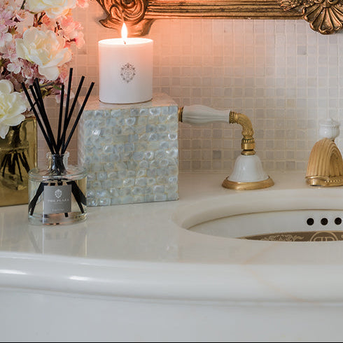 Decorative setup with a candle, diffuser, and decorative mirror on a tiled wall.