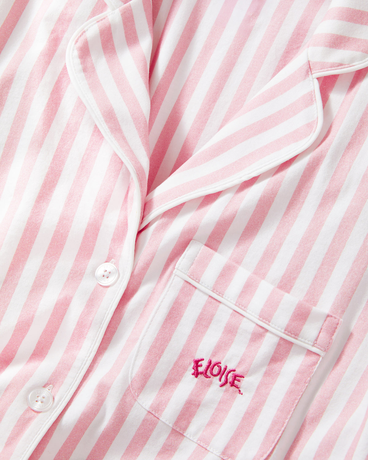 Pink and white striped pajama shirt close-up showing the collar, front buttons, and a chest pocket with pink embroidered text reading 'ELOISE'.