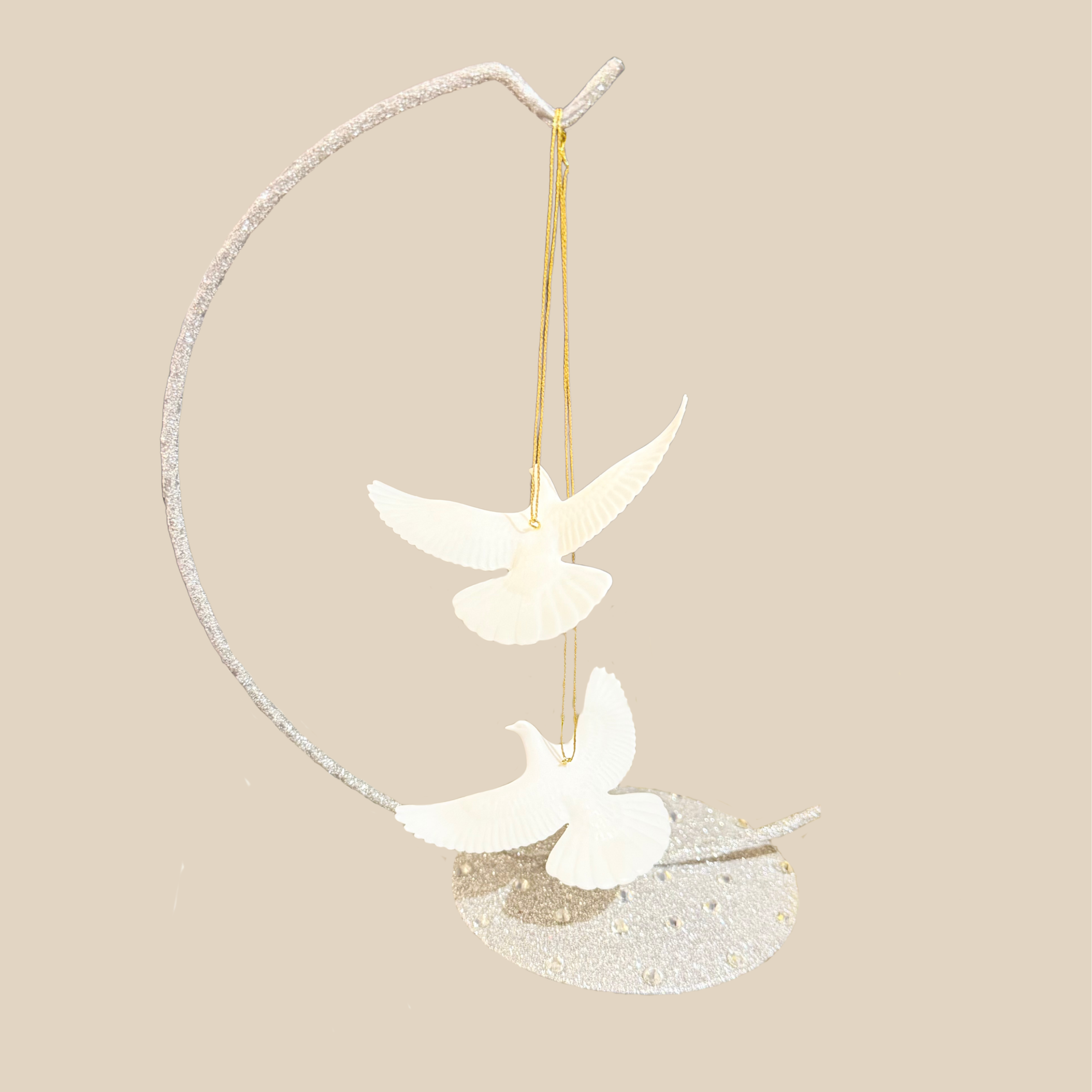 two white turtle dove hanging ornaments featuring two doves suspended from a curved silver branch-like frame on a plain beige background.